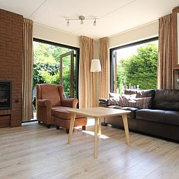 Gezellige woonkamer in Vakantiehuis A 383, De Cocksdorp, Texel. Comfortabele zithoek met uitzicht op groene tuin, ideaal voor ontspanning.