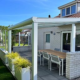 Geniet van de zonnige veranda van Vakantiehuis D 728 in De Cocksdorp, Texel, met een ruim terras en uitzicht op de groene omgeving.