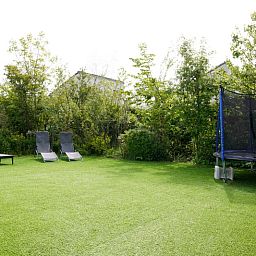Geraeumiger Garten im Ferienhaus D 439 in De Cocksdorp, Texel, mit Liegestuehlen und Trampolin, umgeben von gruener Natur.