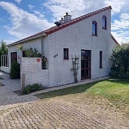 Das Ferienhaus D 489 in De Cocksdorp, Texel, bietet ein charmantes Aeusseres mit einem gruenen Garten und rustikaler Architektur auf den Watteninseln.