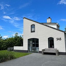 Vakantiehuis E 545 in De Cocksdorp, Texel, met charmante witte gevel en groene omgeving, ideaal voor een ontspannen verblijf op de Waddeneilanden.