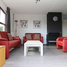 Gezellige woonkamer in Vakantiehuis E 407, De Cocksdorp, Texel, met comfortabele rode banken en moderne inrichting.