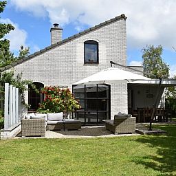 Vakantiehuis F 455 in De Cocksdorp, Texel biedt een charmant terras met comfortabele zithoek en parasol, omgeven door groene natuur.