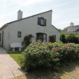 Vakantiehuis E 638 in De Cocksdorp, Texel, omgeven door bloeiende rozenstruiken en een zonnige tuin, ideaal voor een ontspannen verblijf.