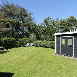 Spacious garden of Holiday Home F 776 in De Cocksdorp, Texel, with green lawn and wooden shed, ideal for relaxation on the Wadden Islands.