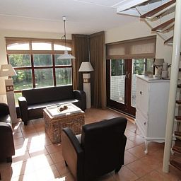 Gemuetliches Wohnzimmer im Ferienhaus F 713 in De Cocksdorp, Texel mit komfortabler Sitzecke und Blick auf die gruene Umgebung.