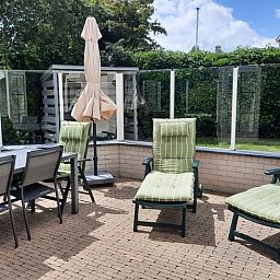 Geniet van het zonnige terras bij Vakantiehuis E 409 in De Cocksdorp, Texel, met comfortabele ligstoelen en een ruime eettafel.