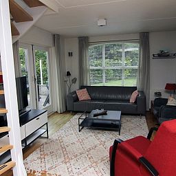 Gemuetliches Wohnzimmer im Ferienhaus E 511, De Cocksdorp, Texel, mit komfortabler Sitzecke und Blick auf die gruene Umgebung.