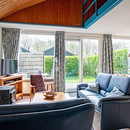 Gezellige woonkamer van Vakantiehuis Slufterhoek 110 in De Cocksdorp, Texel met uitzicht op groene tuin en comfortabele zithoek.