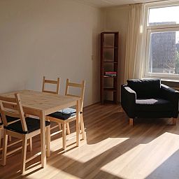 Gemuetliche Essecke im Ferienhaus Kikkerpoel, De Cocksdorp, Texel mit Holztisch und Stuehlen am grossen Fenster.