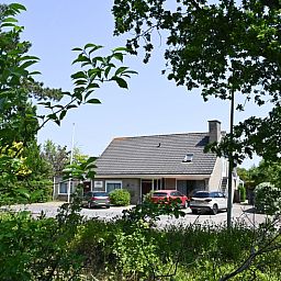 Vooraanzicht van Tesselhuus met zorgvleugel, vakantiehuis in De Koog, Texel, met parkeerplaats en groene omgeving.