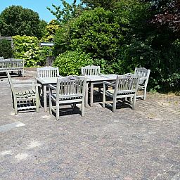 Buitenruimte van Tesselhuus met zorgvleugel in De Koog, Texel, met houten tuinmeubilair en groene omgeving.