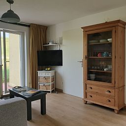 Geraeumiges Wohnzimmer von De Duinpan - Duinhuisje Texel in De Koog, Texel, mit Holzschrank und Fernseher.
