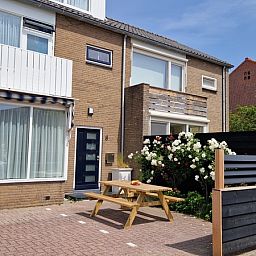 Buitenkant van Vakantiehuis Duinzee Texel in De Koog, met zonnig terras en bloeiende tuin.