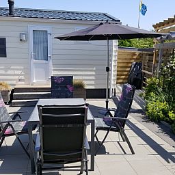 Zonnig terras met parasol en zitplaatsen bij Chalet Bregkoog 138 'Sinne', De Koog, Texel.