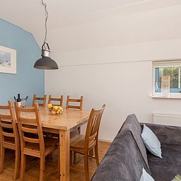 Cozy dining room in bungalow T6AM, De Koog, Texel. Comfortable wooden dining table with six chairs and a modern pendant lamp.