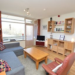 Moderne woonkamer van Appartement Kerckeland 50, De Koog, Texel met uitnodigende zithoek en boekenplanken.
