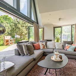 Gemuetliches Wohnzimmer im Ferienhaus in De Koog, Texel, mit grossen Fenstern und Blick auf die Natur, perfekt fuer Entspannung auf den Watteninseln.