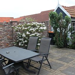Spacious terrace at De Molen, vacation home in Den Burg, Texel, with garden furniture and flowers.