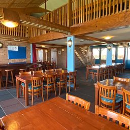 Geraeumiges Esszimmer in De Stolp II rechts, Ferienhaus in Den Hoorn, Texel mit Holztischen und Stuehlen.