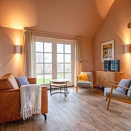 Gemuetliches Wohnzimmer im Ferienhaus Kamille in Den Hoorn auf Texel mit komfortabler Sitzecke und Blick auf die gruene Umgebung.