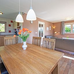Essecke im Ferienhaus 8690 - Junier - Huisman, Sued-Eierland, Texel, mit Holztisch und Blick auf die gruene Umgebung.