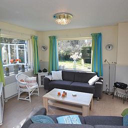 Gezellige woonkamer van Vakantiehuis De Nagtegaal 15, De Wulk in De Dennen, Texel met kleurrijke gordijnen.
