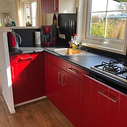 Moderne keuken in Vakantiepark De Bremakker - Akkerveld 14, vakantiehuis in De Dennen, Texel met rode kasten en uitzicht op de natuur.