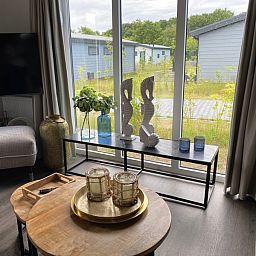 Lichte woonkamer in Vakantiepark de Bremakker - Bosveld 148, De Dennen, Texel met grote ramen en uitzicht op groen.
