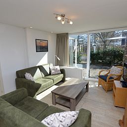 Gemuetliches Wohnzimmer des Ferienhauses de Parel 198 in De Dennen, Texel, mit bequemen gruenen Sofas und viel Tageslicht.