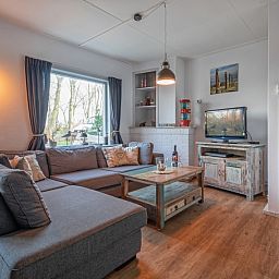 Gemuetliches Wohnzimmer des Ferienhauses Flora in De Dennen, Texel, mit bequemem Sofa und Blick auf die Natur der Watteninseln.