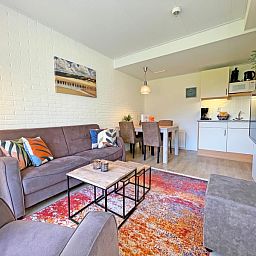 Offenes Wohnzimmer und Kueche im Appartement Bos en Duin 31, De Dennen, Texel mit stilvollen Moebeln und buntem Teppich.