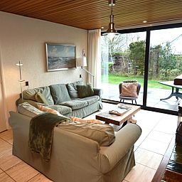 Gemuetliches Wohnzimmer im Holiday home de Parel 258, De Dennen, Texel, mit bequemen Sofas und Blick auf den Garten.