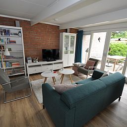 Gezellige woonkamer in Bungalow Verste Coogh 62, De Dennen, Texel met comfortabele zithoek en toegang tot het terras.