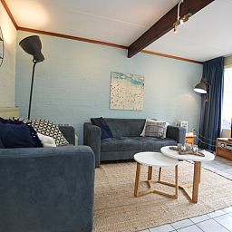 Gezellige woonkamer in Bungalow Verste Coogh 56, De Dennen, Texel, met comfortabele banken en uitzicht op de natuur.