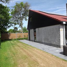 Zijaanzicht van Vakantiehuis Gortersmient 322 in De Dennen, Texel, omgeven door een groene tuin.