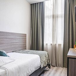 Eenvoudige eenpersoonskamer in Hotel Milano, vakantieappartement in Rotterdam, met knus bed en natuurlijk licht.