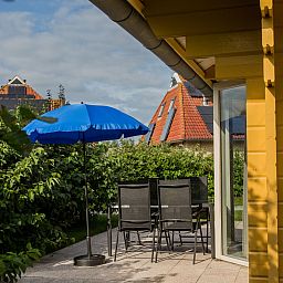 Gezellig terras met blauwe parasol bij Villabungalow, vakantiehuis in Oosterend, Terschelling, omringd door groene hagen op de Waddeneilanden.