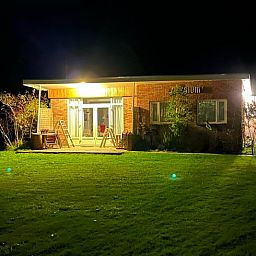 Beleuchtete Abendansicht des Ferienhauses in Midsland Noord, Terschelling, mit einladender Terrasse und gruener Umgebung auf den Watteninseln.
