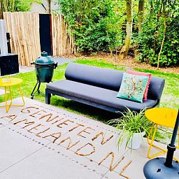 Aussenlounge im Ferienhaus in Ballum, Ameland, mit bequemen Sitzgelegenheiten und gruener Umgebung, ideal zum Entspannen.