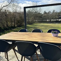 Houten eettafel op het terras van Zeevonk vakantiehuis in Ballum, Ameland, met uitzicht op de groene omgeving.