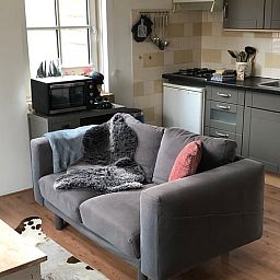 Comfortabele woonkamer in Vakantiehuisje in Buren Ameland met knusse bank en open keuken, ideaal voor ontspanning.