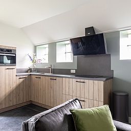 Moderne keuken in De Deel, appartement in Hollum, Ameland, met strakke houten kasten en veel lichtinval.