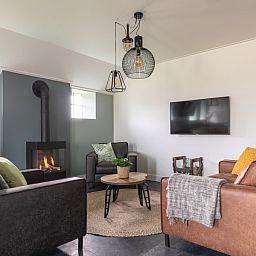 Comfortabele woonkamer van De Deel, appartement in Hollum, Ameland, met leren banken en een gezellige open haard.