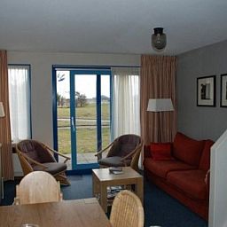 Gezellige woonkamer in Amelander Kaap nr. 54, een appartement in Hollum, Ameland met comfortabele zitruimte en uitzicht op de groene omgeving.