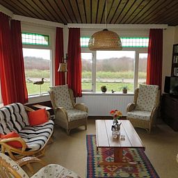 Gemuetliches Wohnzimmer des Ferienhauses Zeerust auf Schiermonnikoog, mit Korbmoebeln und Blick auf die Natur des Wattenmeeres.