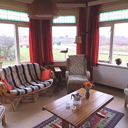 Gemuetliche Sitzecke im Ferienhaus Zeerust auf Schiermonnikoog, Watteninseln, mit Blick auf die Natur und bequemen Rattanmoebeln.