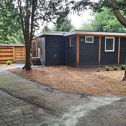 Rustic exterior of Cottage in Gasselte, Drenthe, surrounded by trees and a charming wooden fence.