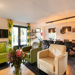 Gemuetliches Wohnzimmer der Zandduin Villa mit Sauna 10 in Hooghalen, Drenthe, mit bequemen Stuehlen und Blick auf den Garten.