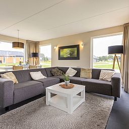 Spacious living room in bungalow Drentsche Aa 6, Tynaarlo, North Drenthe, with comfortable sofa and view of green surroundings.